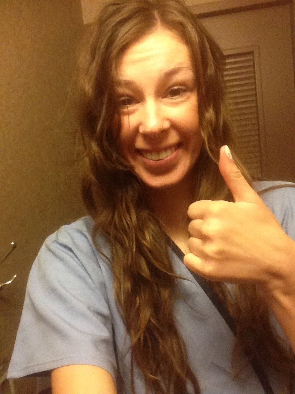 Jenna wearing blue medical gown inside the dressing room giving a thumbs up