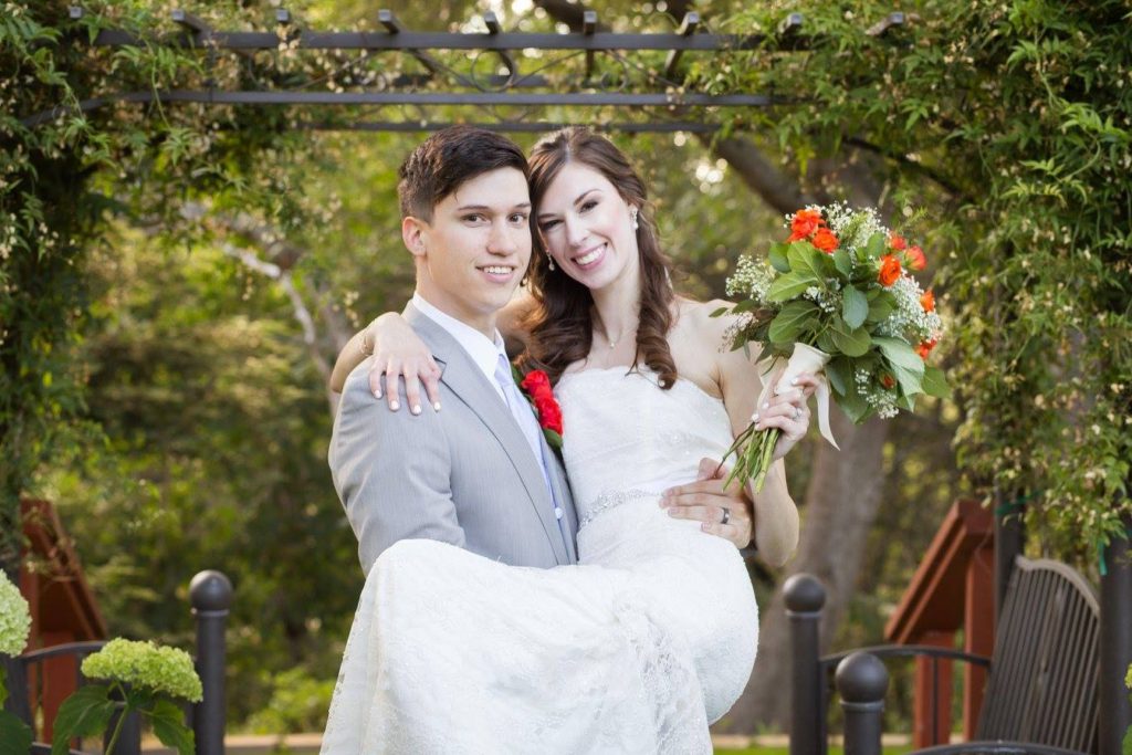 Groom Tyler in a light grey suit holding Jenna in a white, strapless wedding dress holding a bouquet of white and orange flowers