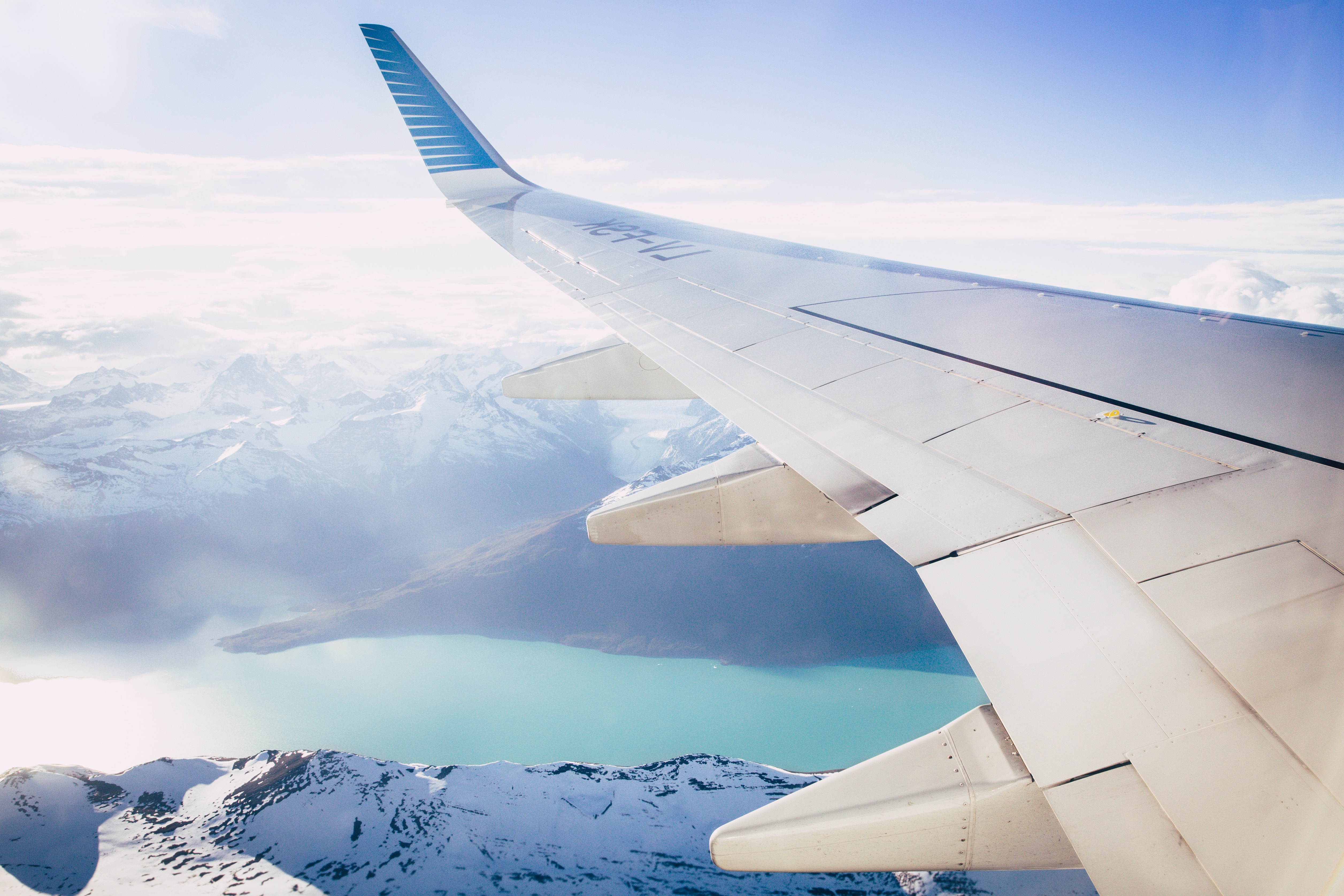White airplane wing over river and snowy mountains
