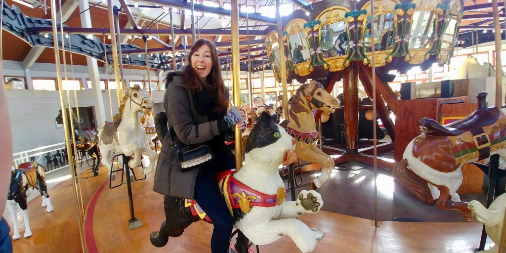 Jenna in a winter jacket riding on a cat on a carousel 