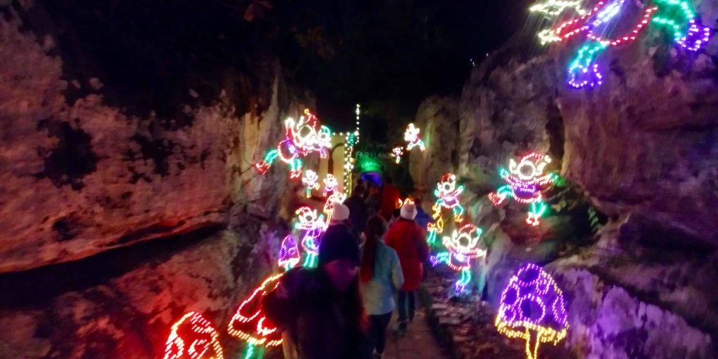 Line of people walking through caves decorated with neon Christmas lights
