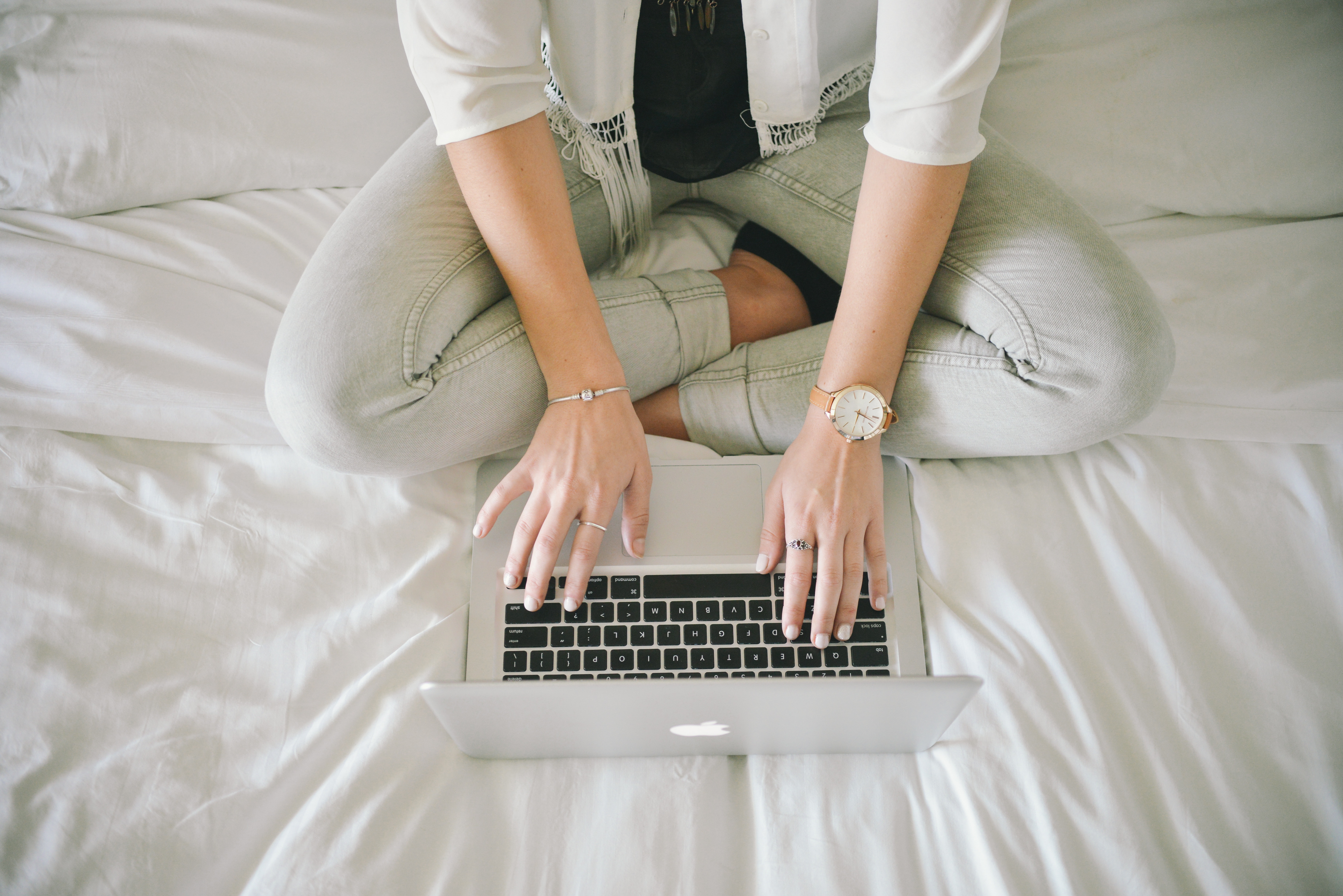 Women sitting in white bed typing on laptop keyboard