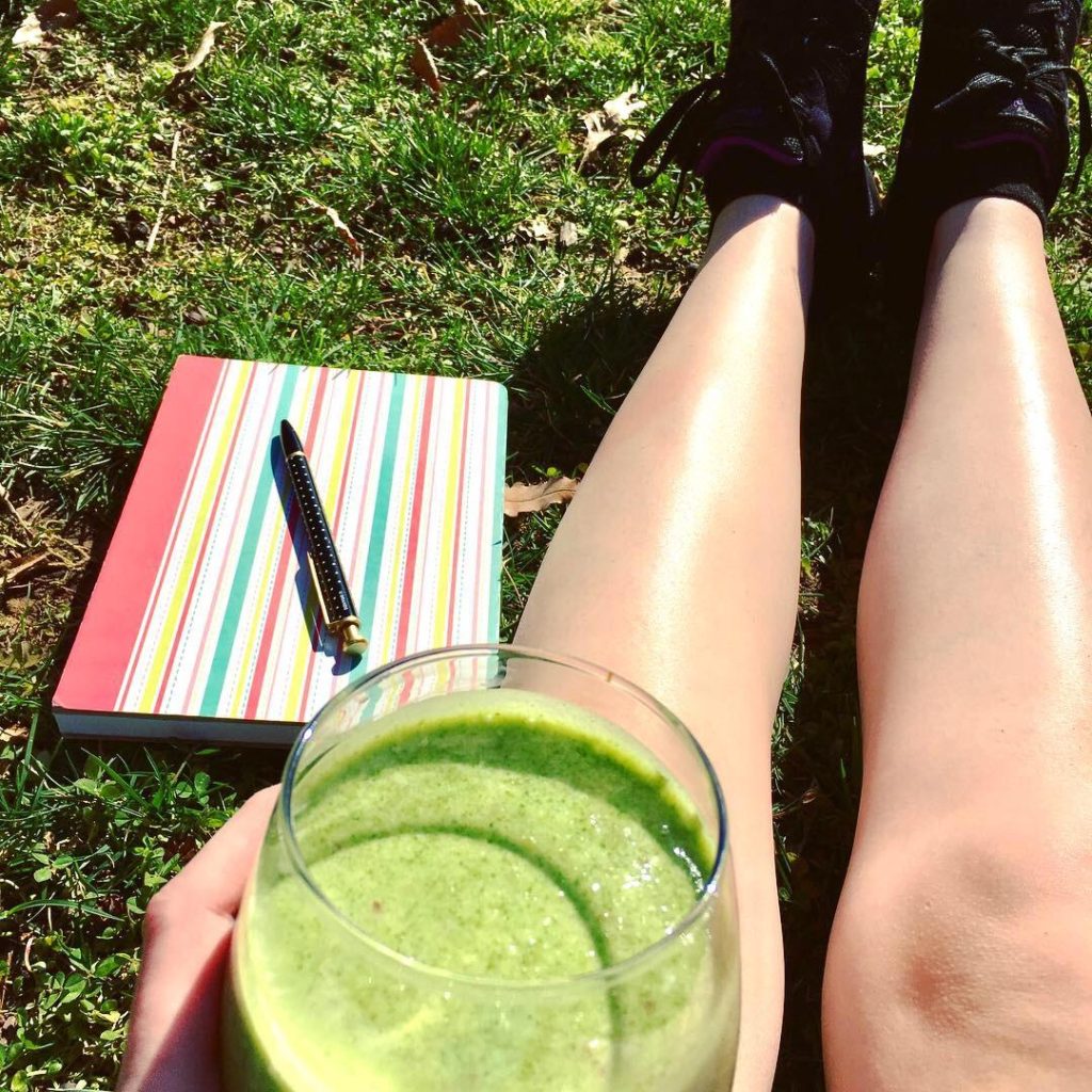 Jenna sitting in grass next to notebook and holding a smoothie