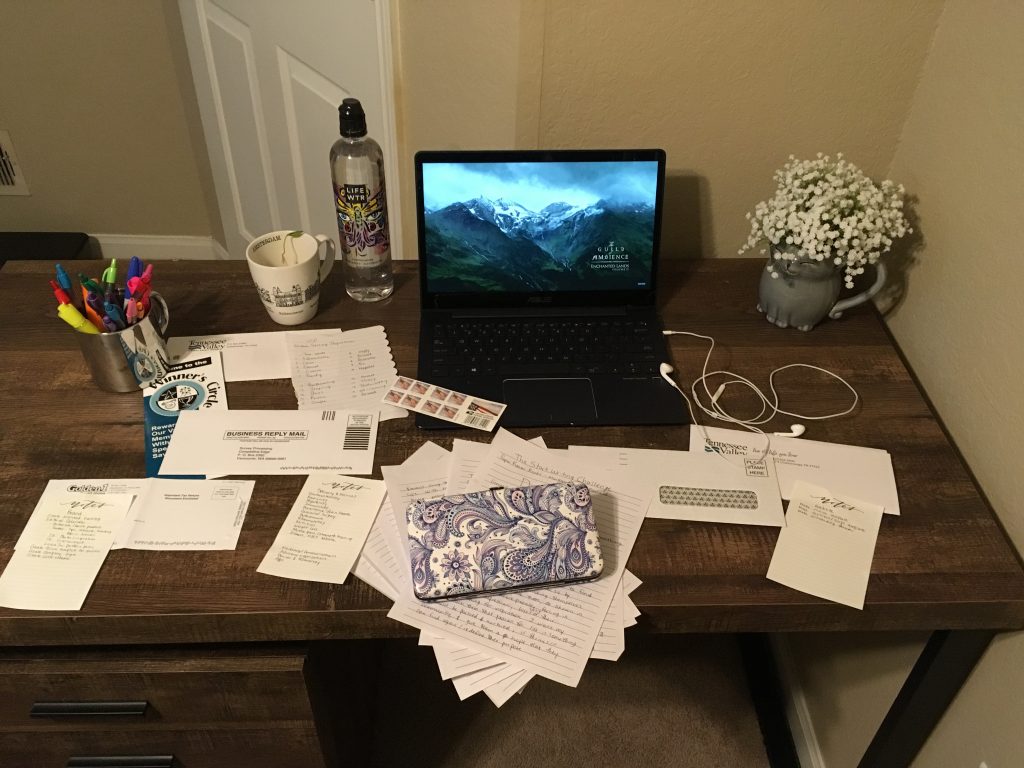 Jenna's messy desk with piles of paperwork beside laptop, headphones, tea, pens, and a water bottle