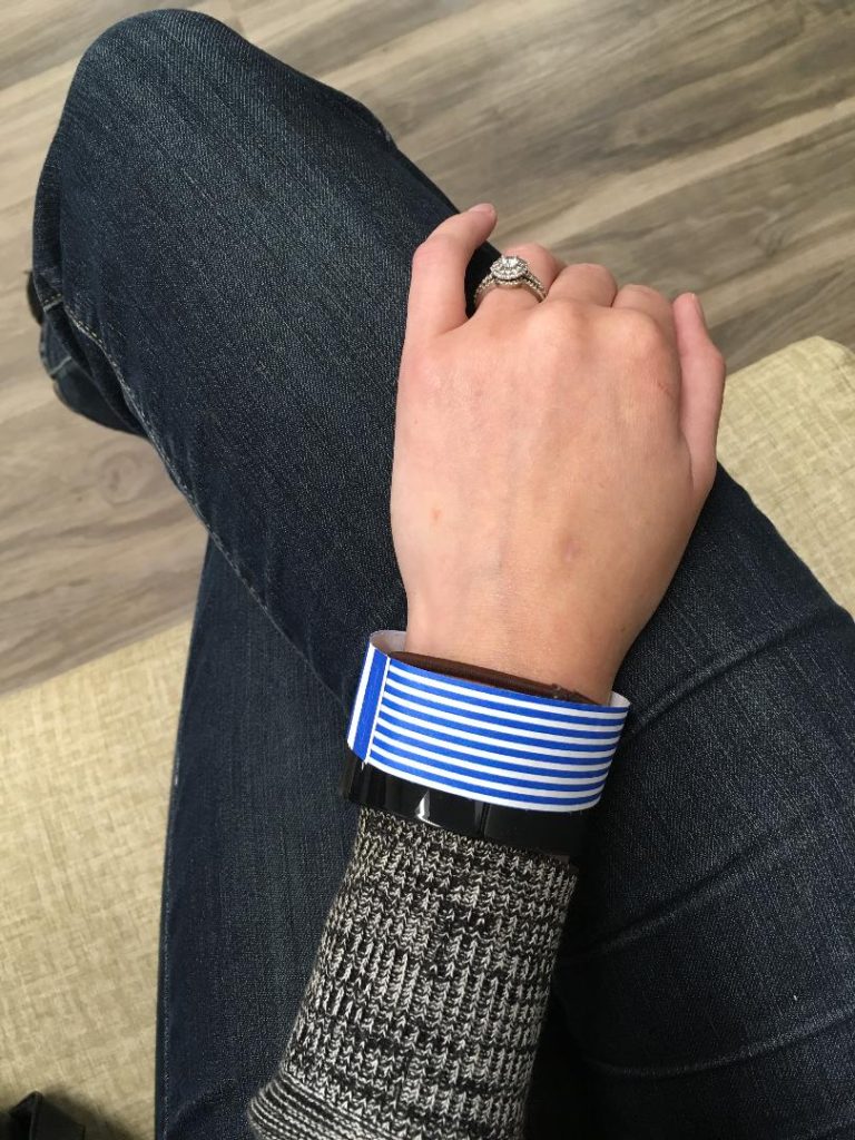 Jenna resting hand on leg with blue and white striped hospital bracelet