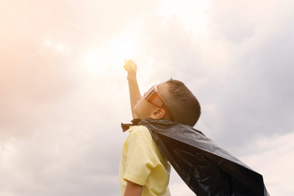 Boy wearing sunglasses and trash bag as a cape pumping fist into sky like a superhero